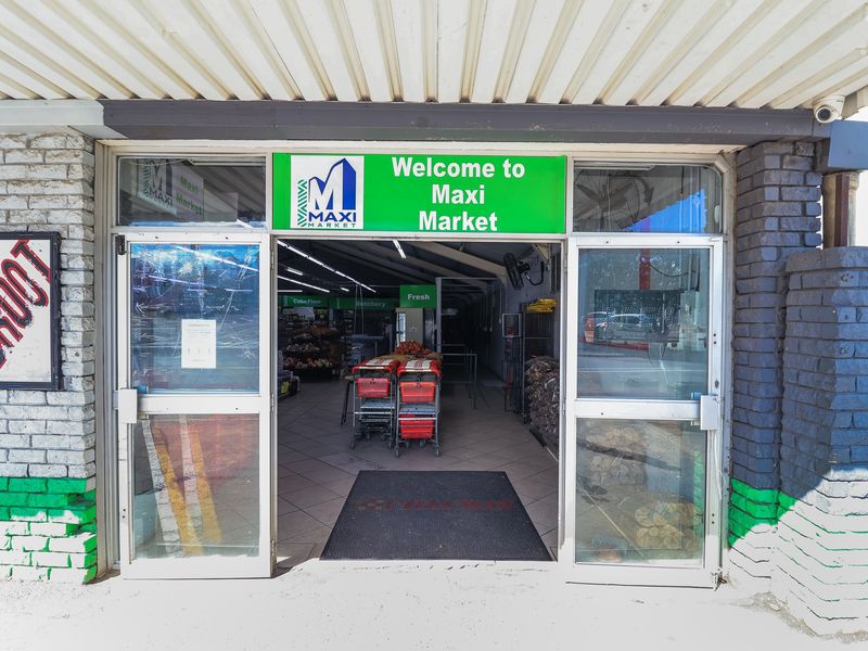 Front entrance of a retail market featuring glass doors, painted brick facade, and a corrugated metal awning.