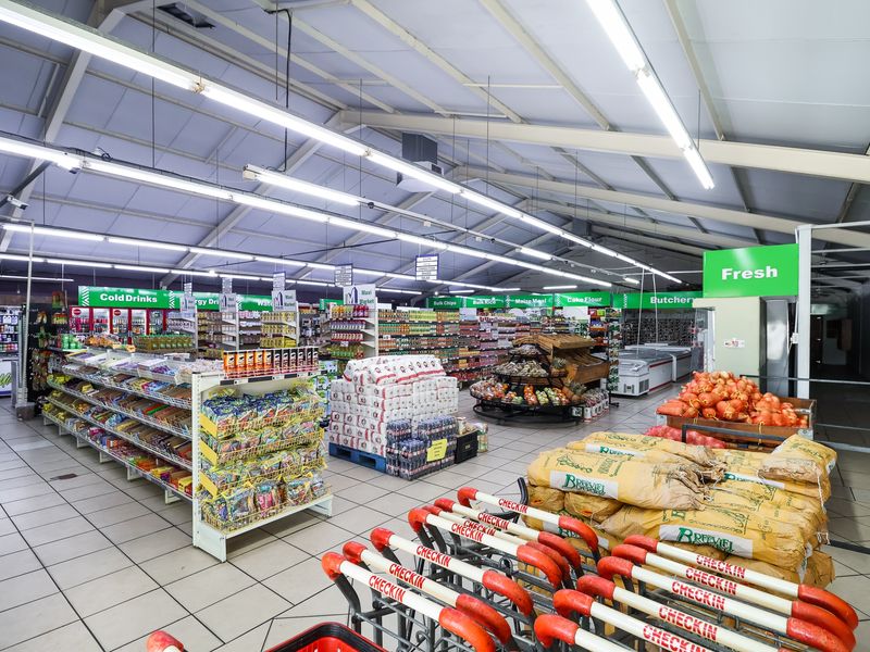 Spacious retail floor area featuring high ceilings with exposed steel trusses, bright fluorescent lighting, and durable tiled flooring throughout the shopping space.