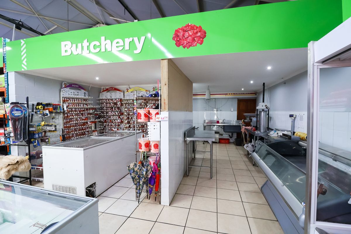 A functional butchery retail space featuring tiled flooring, stainless steel prep surfaces, and commercial refrigeration units within a partitioned commercial environment.