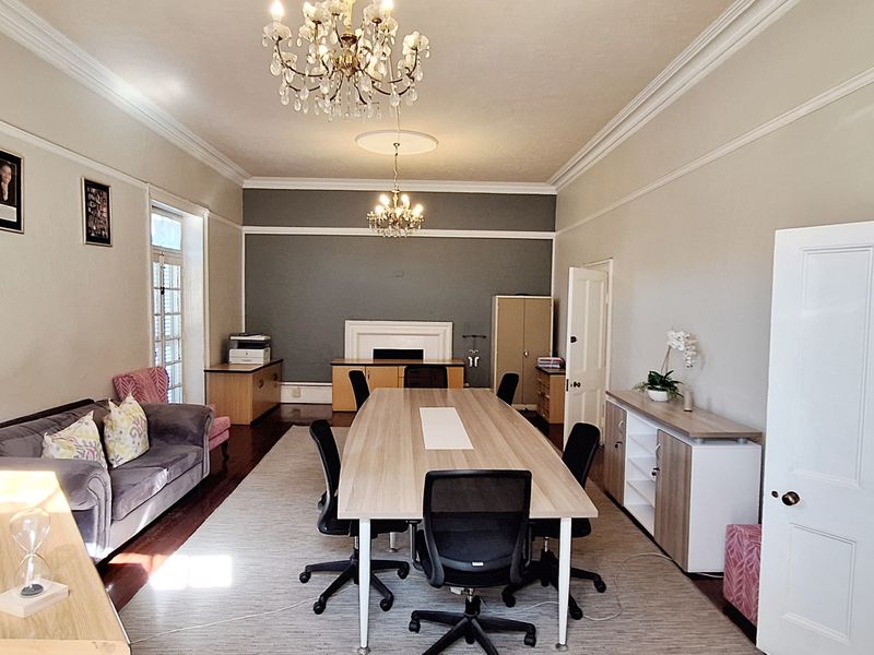 A spacious, well-lit office featuring elegant crown molding, dual crystal chandeliers, and a central fireplace, providing a professional and sophisticated workspace environment.