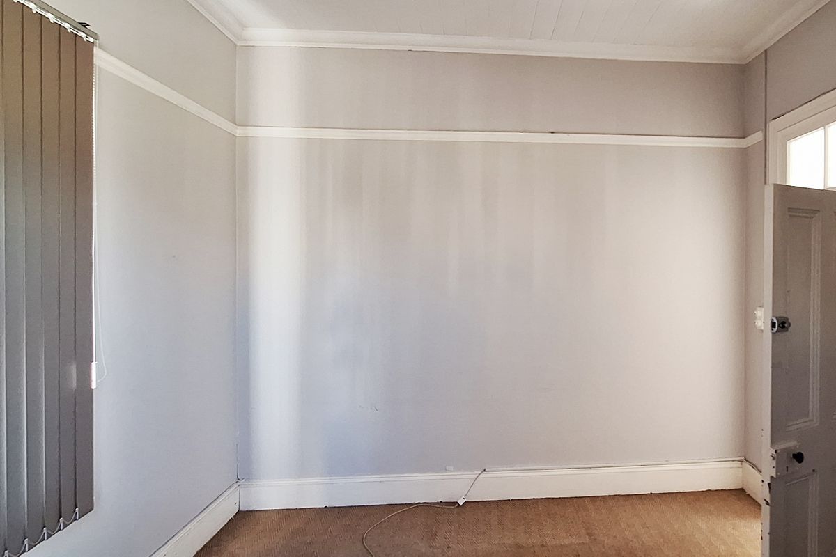 An empty bedroom featuring neutral walls, vertical blinds, and classic architectural details like picture rails and skirting boards.