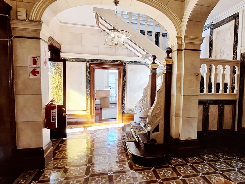 Grand entrance foyer featuring ornate stone archways, decorative tile flooring, and a classic staircase with detailed balustrades in a well-maintained commercial space.