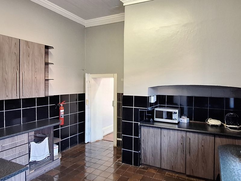 A functional commercial kitchen featuring dark laminate cabinetry, black tiled splashbacks, and durable tiled flooring with a classic crown molding finish.