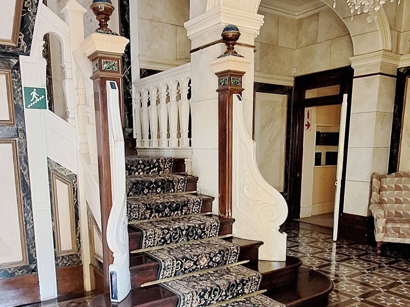Grand entrance hall featuring ornate wooden staircase, decorative tiled flooring, and elegant arched architectural details, showcasing classic craftsmanship and character.