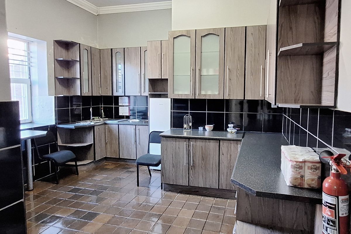A functional commercial kitchen featuring wood-grain cabinetry, dark tiled backsplash, and durable tiled flooring, providing a practical workspace for staff.