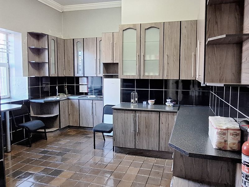 A functional commercial kitchen featuring wood-grain cabinetry, dark tiled backsplash, and durable tiled flooring, providing a practical workspace for staff.