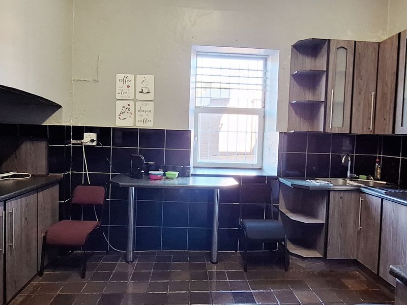A functional kitchen featuring dark tiled backsplashes, laminate cabinetry, and tiled flooring, providing a practical workspace with integrated sink and storage.