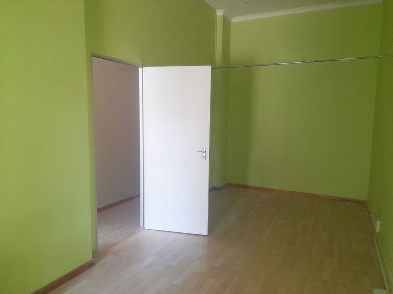 An empty, vacant room featuring laminate flooring, bright green painted walls, and a standard internal door leading to an adjacent space.