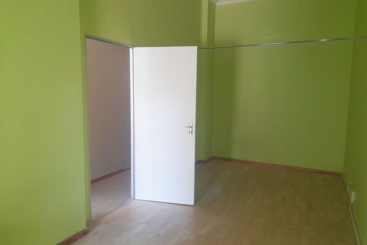 An empty, vacant room featuring laminate flooring, bright green painted walls, and a standard internal door leading to an adjacent space.