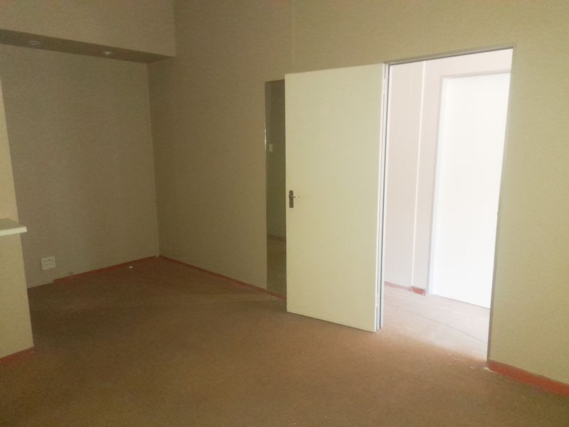 An empty, carpeted interior space with neutral walls and an open doorway leading to an adjacent room.