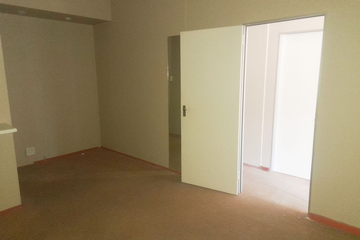 An empty, carpeted interior space with neutral walls and an open doorway leading to an adjacent room.