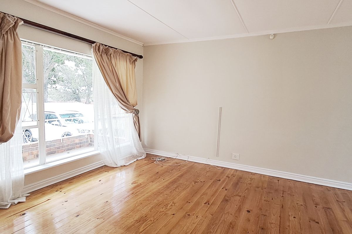 A bright and spacious living room featuring polished hardwood flooring, large windows, and neutral wall finishes, offering a versatile blank canvas.