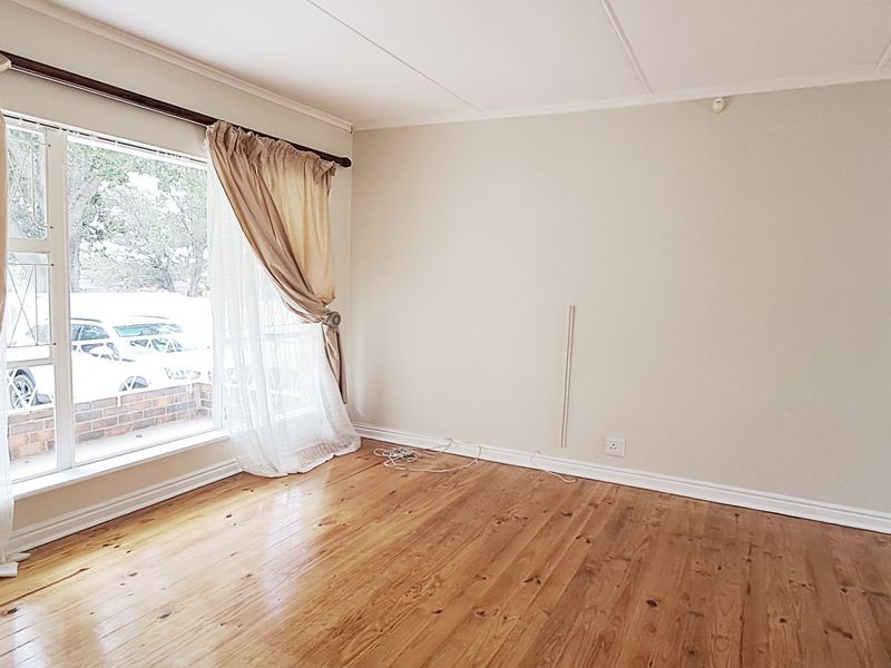 A bright and spacious living room featuring polished hardwood flooring, large windows, and neutral wall finishes, offering a versatile blank canvas.