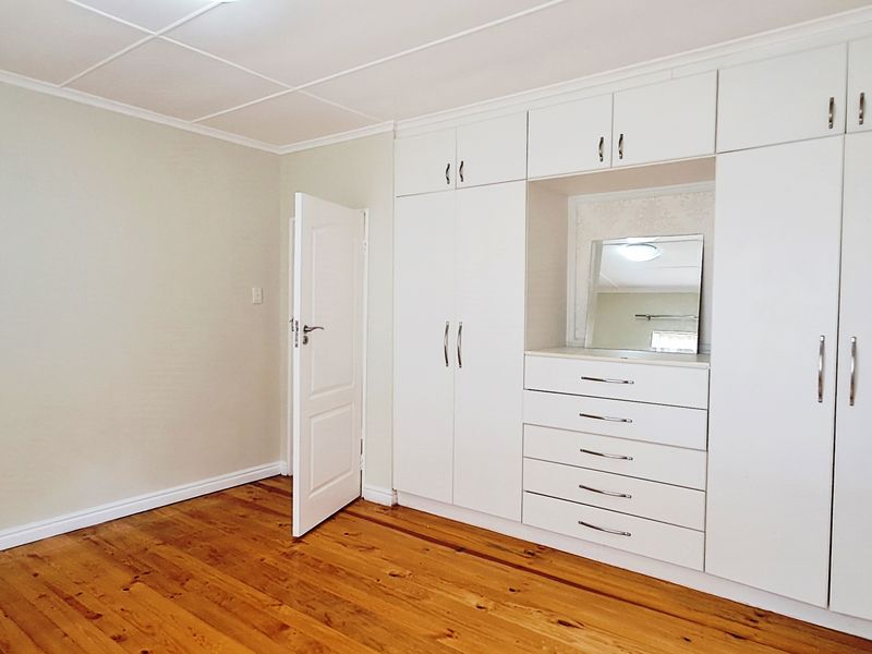 A bright, empty bedroom featuring polished wooden flooring, neutral walls, and extensive white built-in cabinetry with integrated drawer storage.