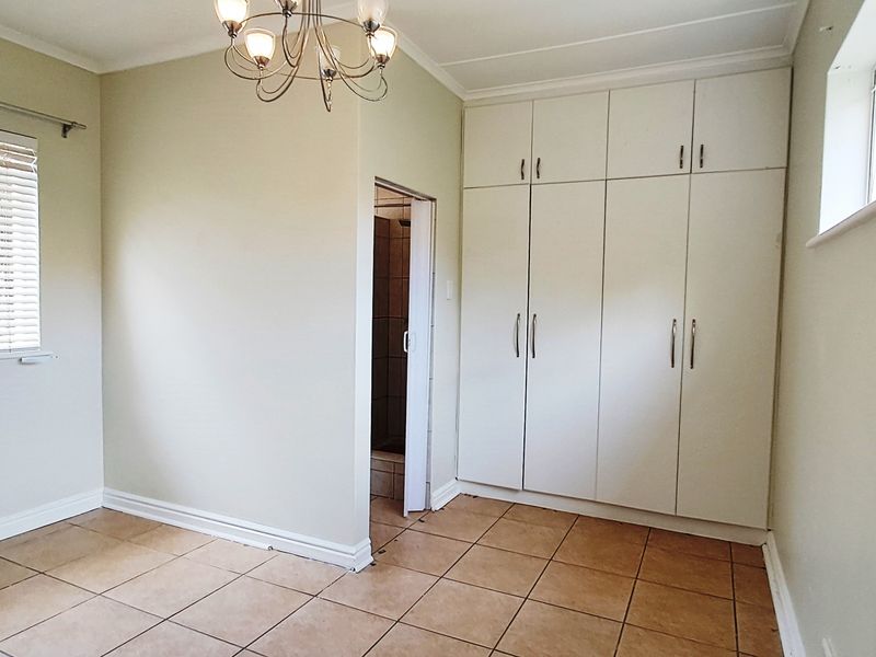 A clean, empty bedroom featuring tiled flooring, built-in cupboards, and an en-suite bathroom access point.