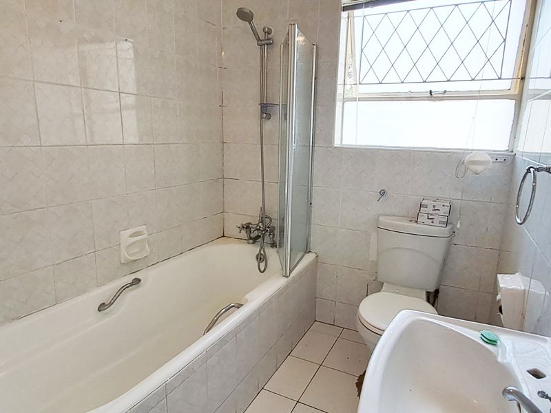 A dated bathroom featuring a bathtub with shower attachment, pedestal basin, and toilet, finished with original wall and floor tiling.