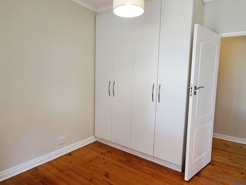 A bright, empty bedroom featuring polished timber flooring and ample built-in cupboard storage space.