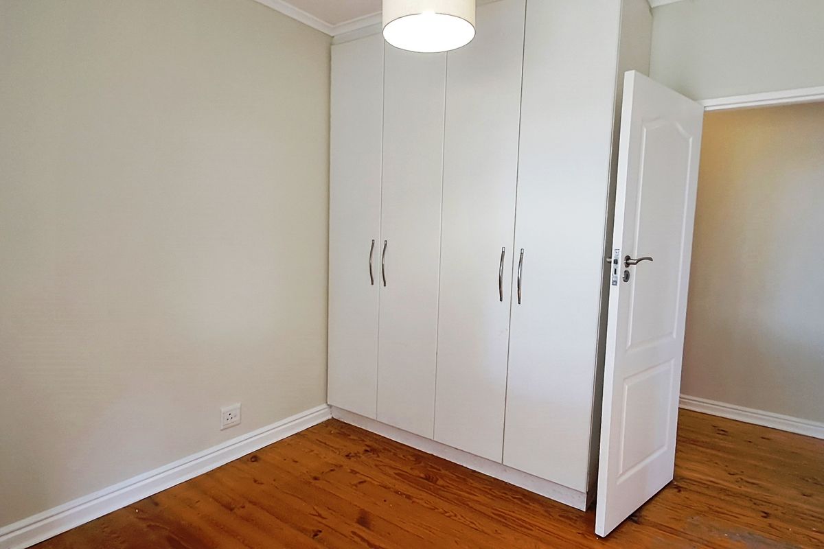 A bright, empty bedroom featuring polished timber flooring and ample built-in cupboard storage space.