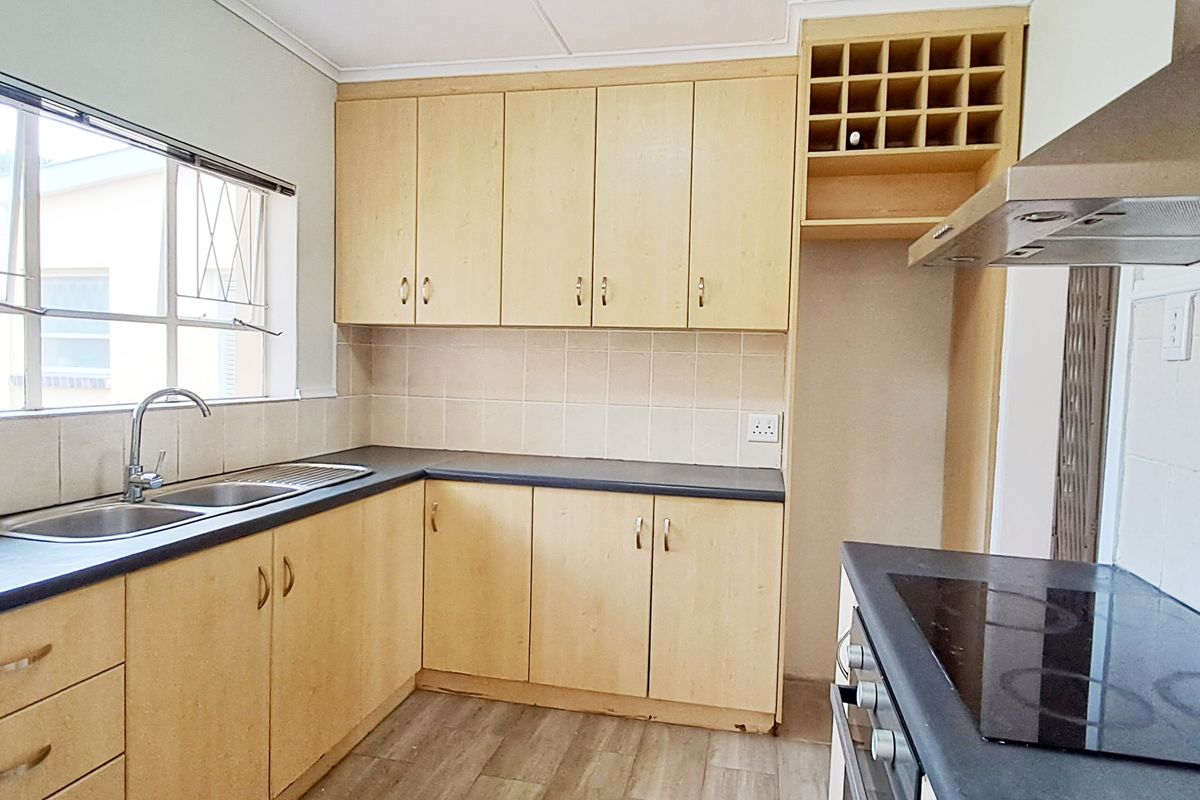 A functional kitchen featuring light wood-finish cabinetry, dark countertops, a built-in oven and hob, and a tiled backsplash with a window view.