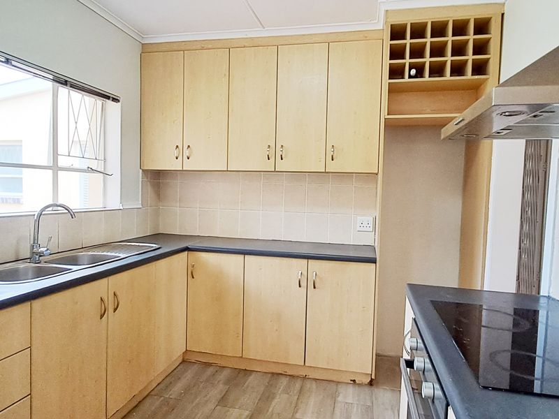 A functional kitchen featuring light wood-finish cabinetry, dark countertops, a built-in oven and hob, and a tiled backsplash with a window view.