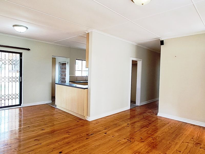 Spacious open-plan living area featuring polished hardwood floors, a kitchen peninsula, and a sliding glass door with security gate leading to the exterior.