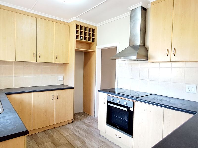 A functional kitchen featuring light wood-tone cabinetry, dark countertops, a built-in oven with electric hob, and a stainless steel extractor fan.