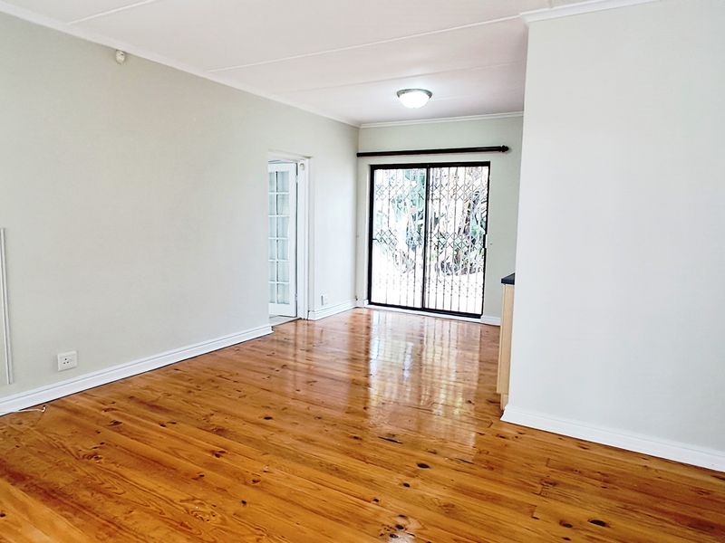 A bright, empty living area featuring polished hardwood flooring, neutral walls, and a sliding glass door with a security gate leading outdoors.