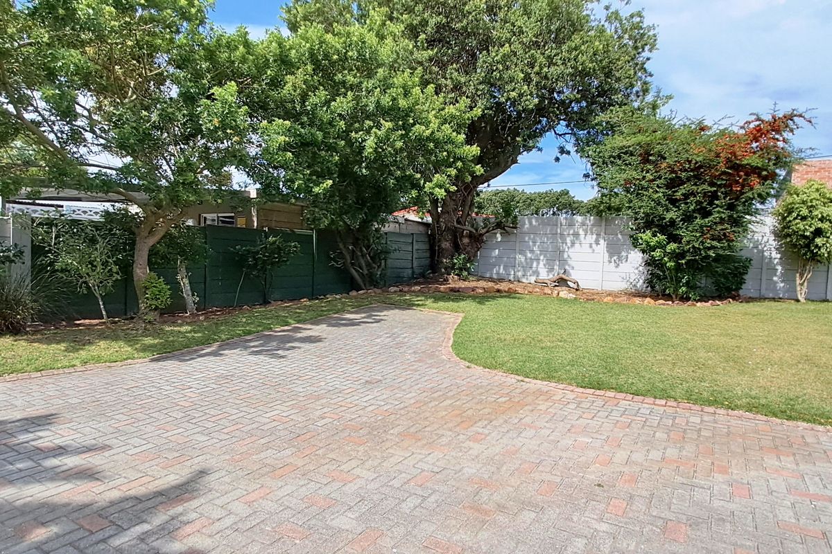 A spacious rear garden featuring a paved area, established trees, and a secure perimeter wall.