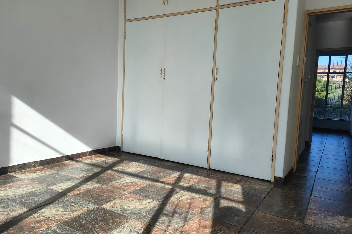 A bedroom featuring built-in cupboards and tiled flooring, with a view into the adjacent hallway.