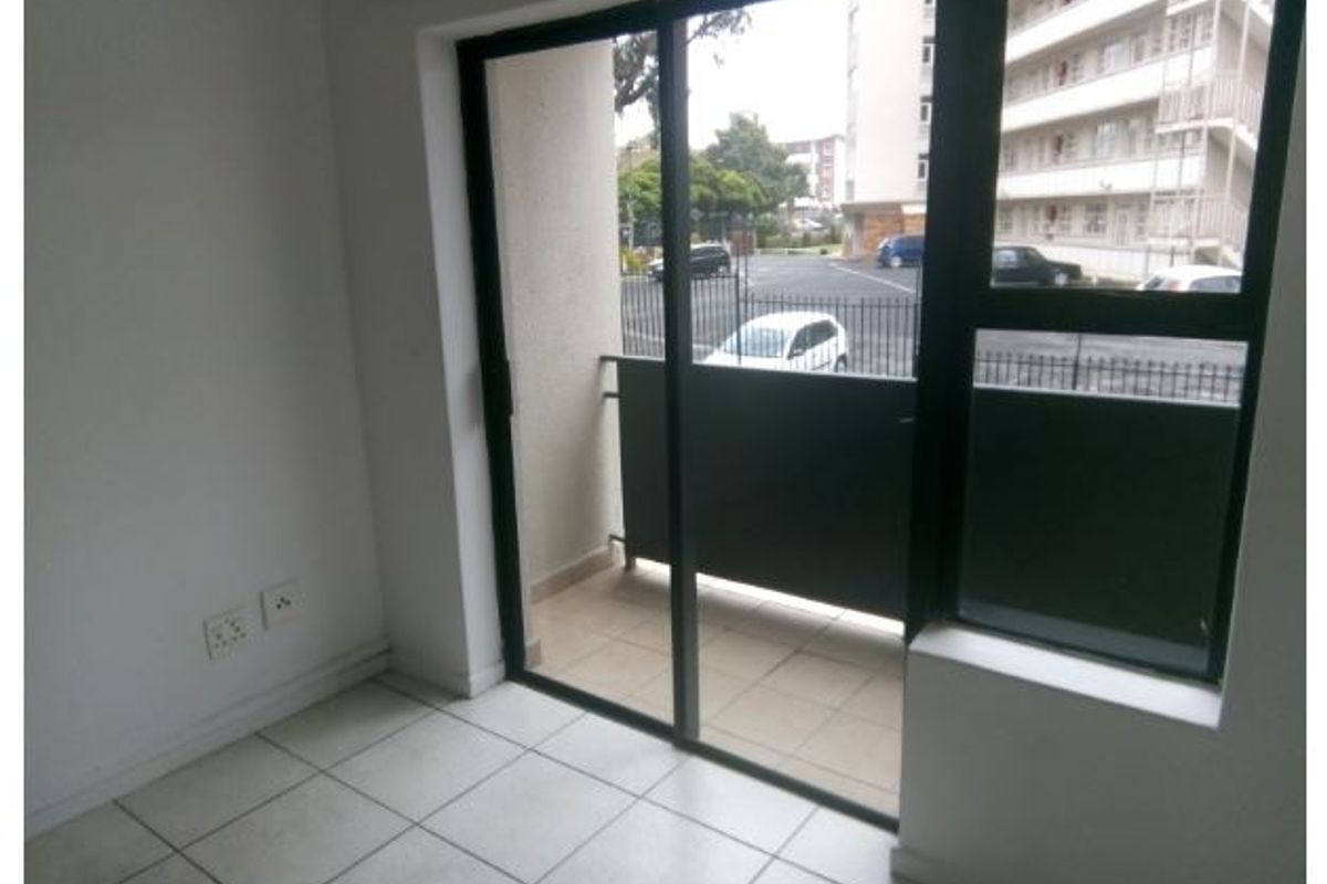 An empty living area featuring tiled flooring and a sliding glass door that opens onto a small balcony.