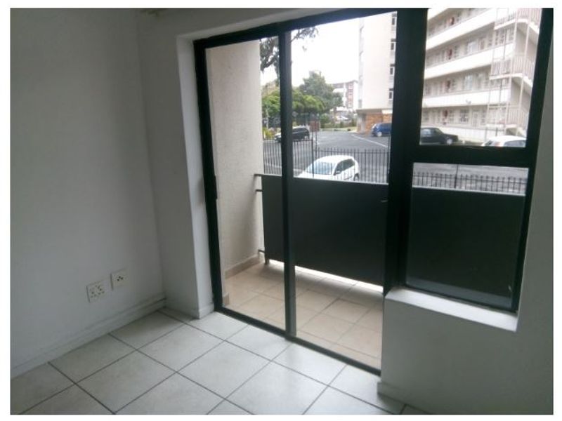 An empty living area featuring tiled flooring and a sliding glass door that opens onto a small balcony.