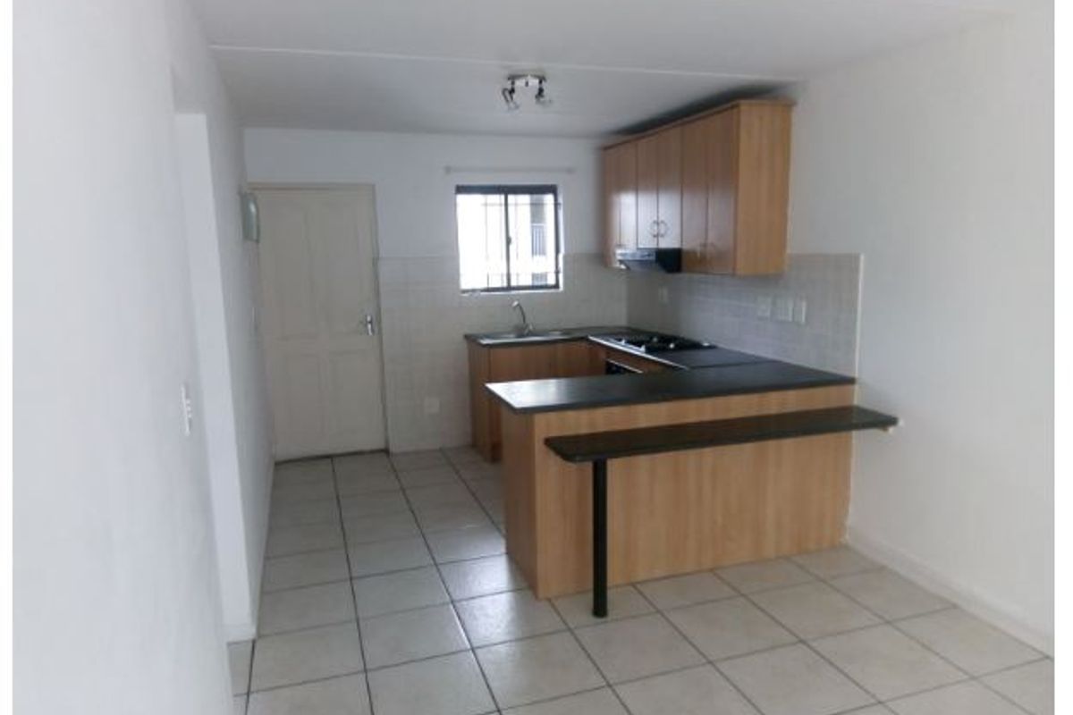 A functional kitchen featuring light wood cabinetry, dark laminate countertops, a breakfast bar, and tiled flooring, offering a clean and practical layout.