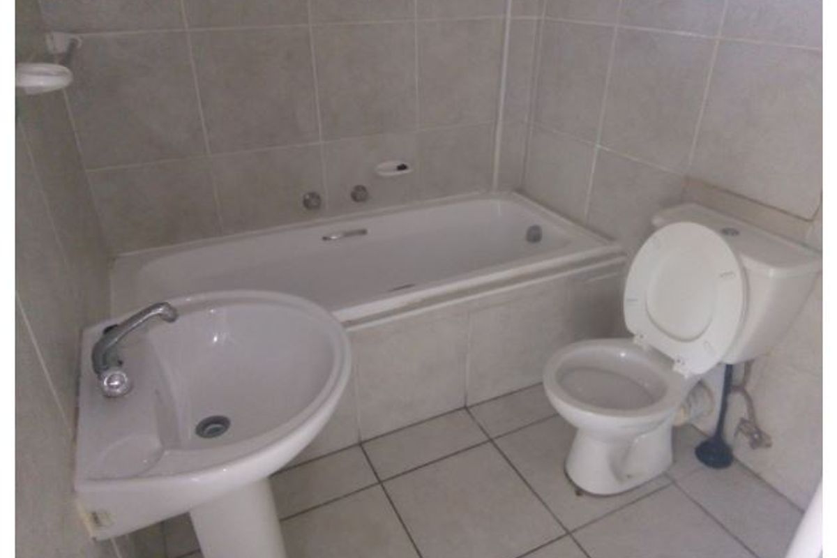 A functional bathroom featuring a pedestal basin, built-in bathtub, and toilet with neutral ceramic tiling throughout.