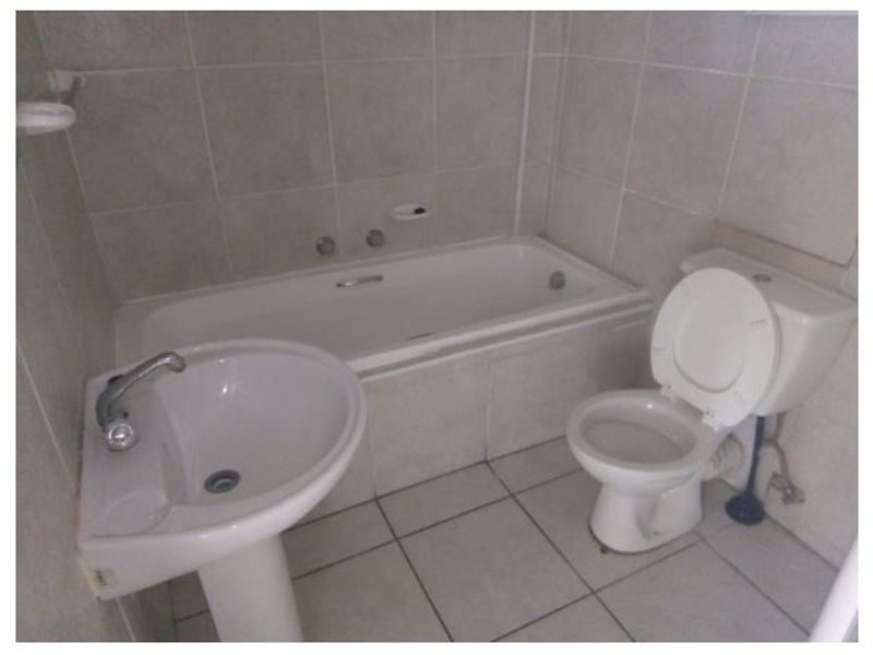 A functional bathroom featuring a pedestal basin, built-in bathtub, and toilet with neutral ceramic tiling throughout.