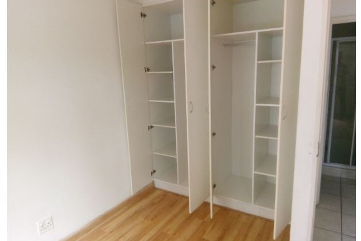 A clean, empty bedroom featuring light-toned laminate flooring and white built-in cupboards with ample shelving and hanging space.