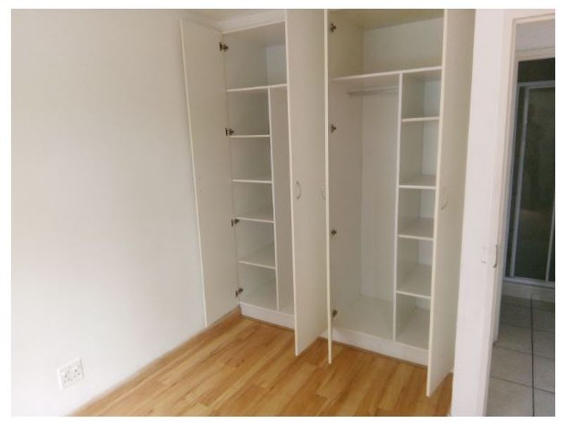A clean, empty bedroom featuring light-toned laminate flooring and white built-in cupboards with ample shelving and hanging space.