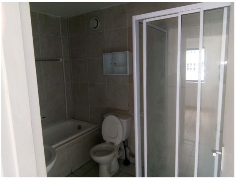 A functional bathroom featuring a bathtub, separate shower enclosure, and toilet, finished with neutral wall and floor tiles.