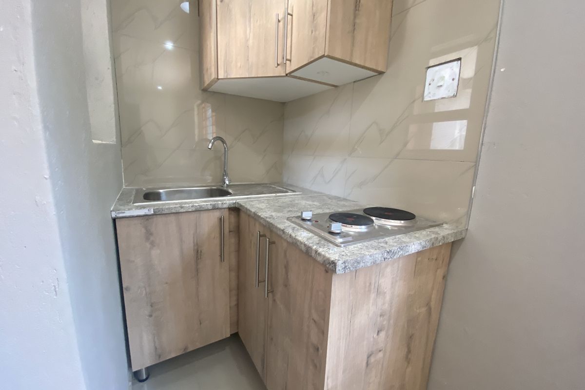 Compact kitchenette featuring wood-look cabinetry, stone-effect countertops, a stainless steel sink, and a built-in electric hob with tiled backsplash.
