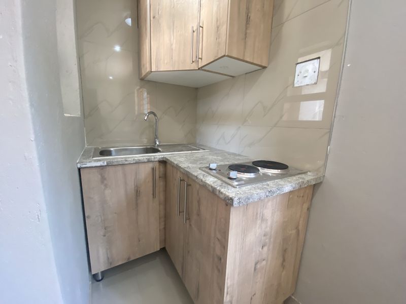 Compact kitchenette featuring wood-look cabinetry, stone-effect countertops, a stainless steel sink, and a built-in electric hob with tiled backsplash.