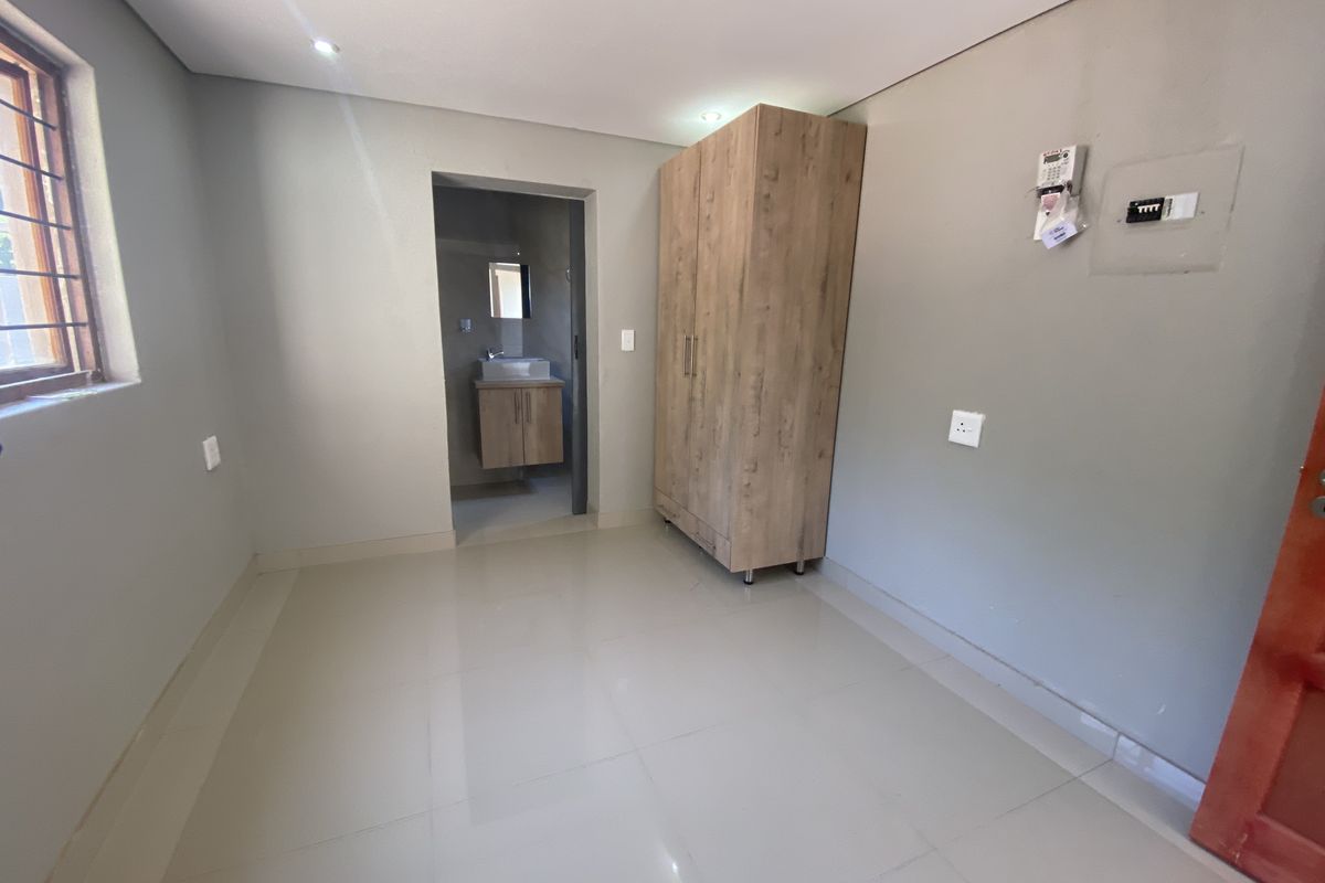 A clean, modern bedroom featuring tiled floors, recessed lighting, a built-in wardrobe, and an en-suite bathroom access.
