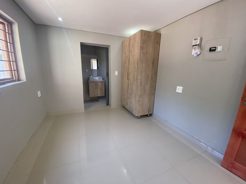 A clean, modern bedroom featuring tiled floors, recessed lighting, a built-in wardrobe, and an en-suite bathroom access.
