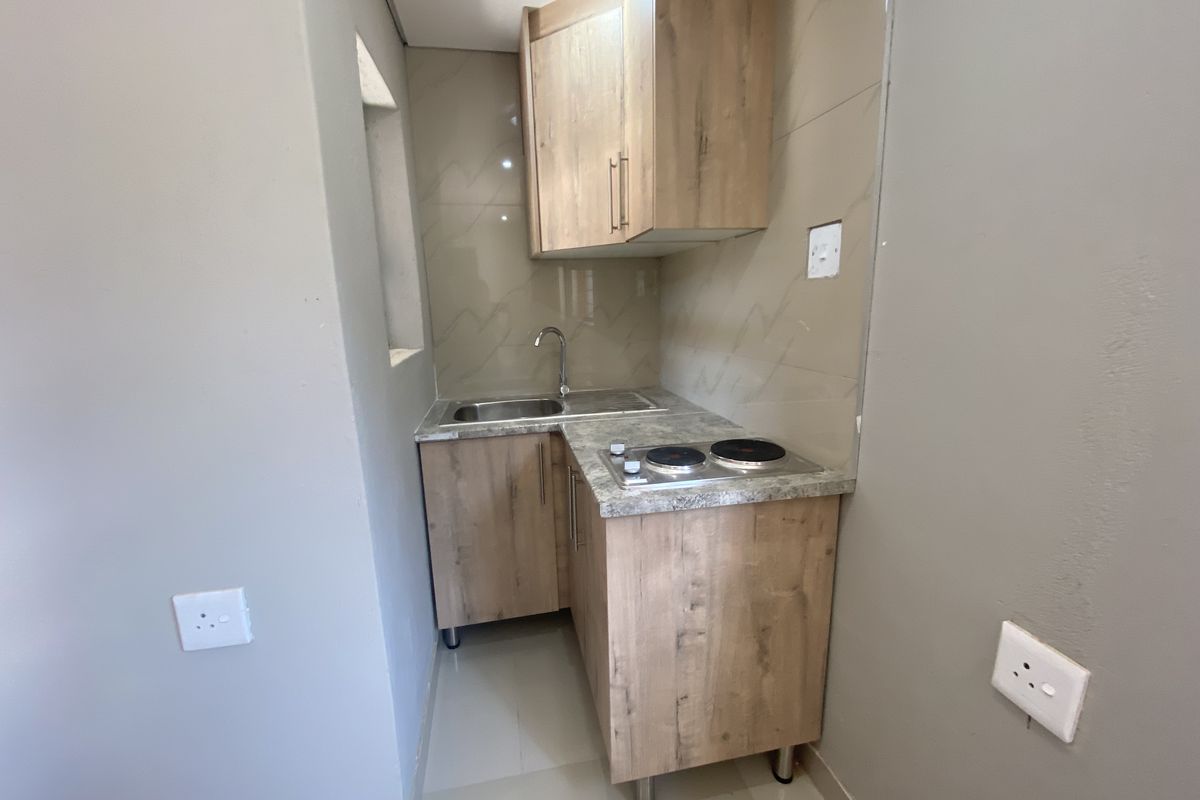 A compact, modern kitchenette featuring wood-finish cabinetry, a stainless steel sink, and a built-in electric hob with tiled splashback.