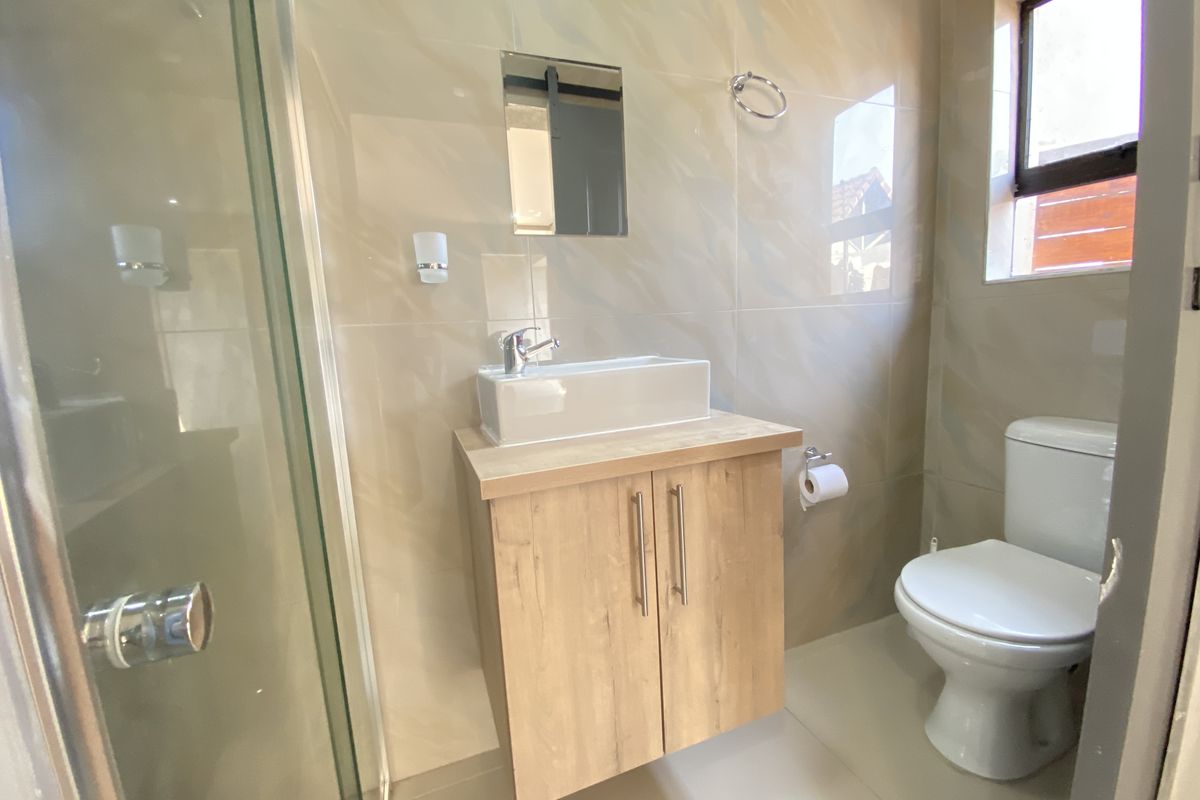 A modern, well-maintained bathroom featuring a floating vanity with a vessel sink, a glass-enclosed shower, and neutral wall tiling.