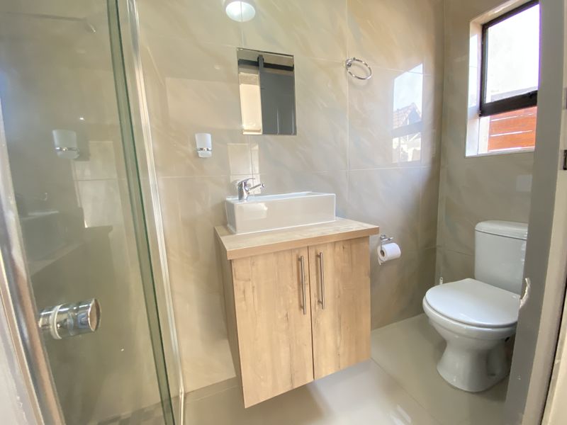 A modern, well-maintained bathroom featuring a floating vanity with a vessel sink, a glass-enclosed shower, and neutral wall tiling.
