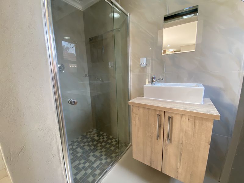 Modern bathroom featuring a glass-enclosed shower, a contemporary wall-mounted vanity with a vessel sink, and neutral wall tiling.