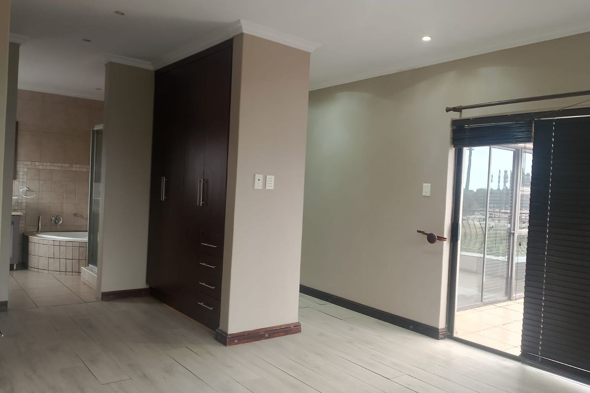 Spacious bedroom featuring built-in cupboards, light wood-look flooring, and direct access to a private balcony, with an adjoining en-suite bathroom.