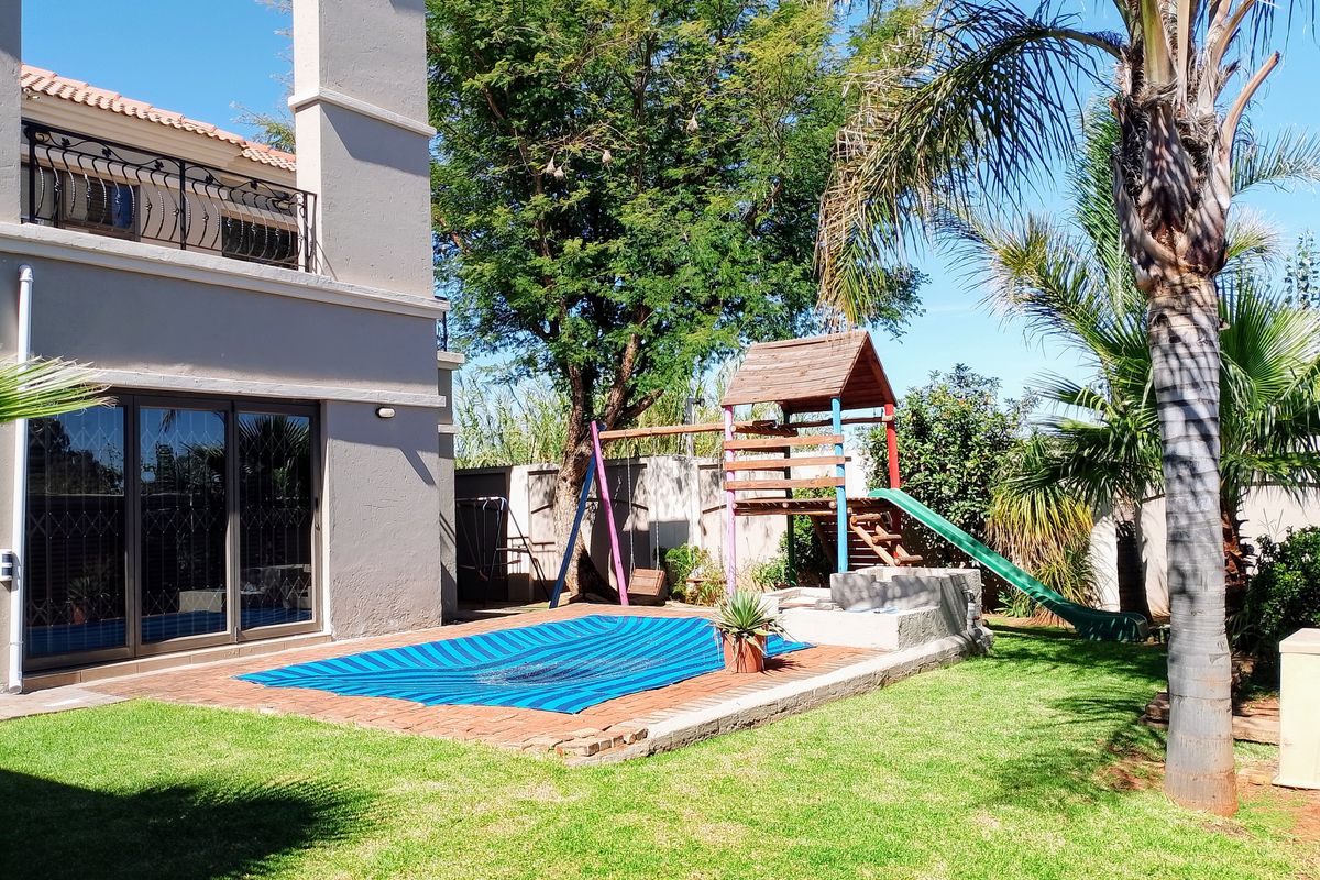 Rear garden area featuring a swimming pool with a safety cover, paved surround, and a two-story house elevation with a balcony.