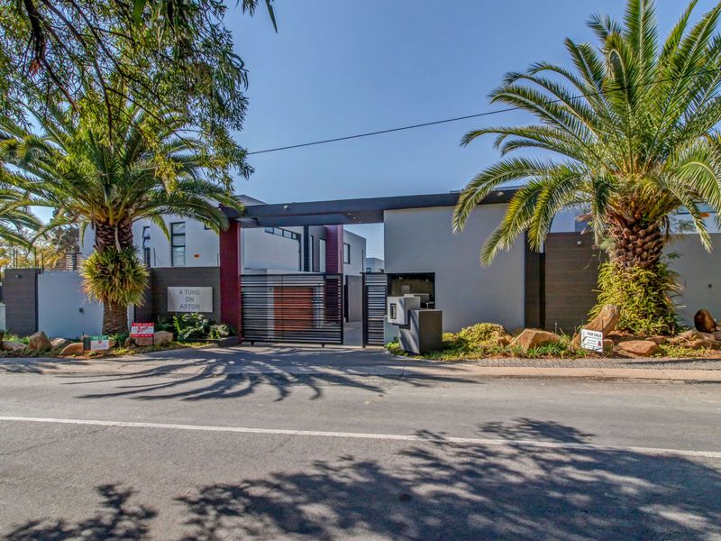 Modern townhouse complex entrance featuring a secure sliding gate, intercom system, and well-maintained landscaped garden with mature palm trees.