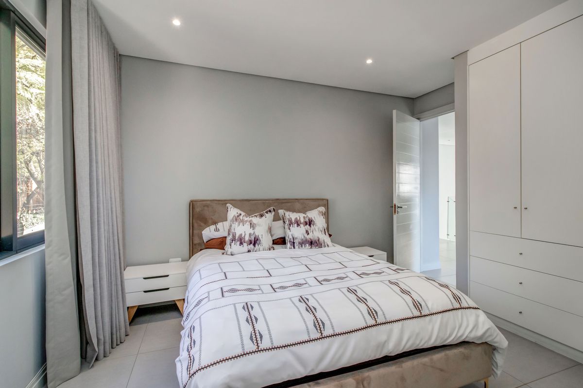 Modern bedroom featuring neutral grey walls, tiled flooring, recessed downlighting, and ample built-in cupboard storage.