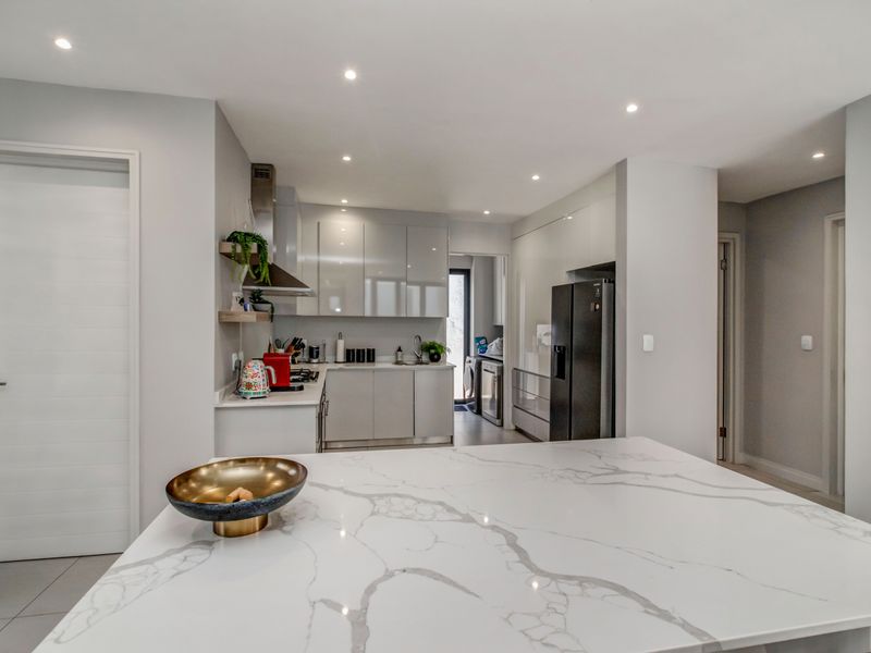 Modern kitchen featuring high-gloss cabinetry, a large marble-look quartz island, and integrated appliances with recessed ceiling lighting.